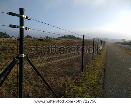 VELUWE, THE NETHERLANDS - DECEMBER 2016: Fence alongside cycle path and road through Veluwe national park, to prevent wildlife vehicle collisions   Royalty-Free Stock Photo #589722950