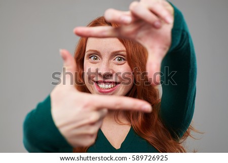Close-up shot of positive female with auburn hair making a frame with fingers. Picture framing concept
