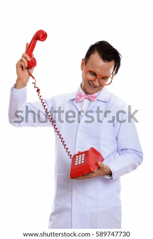 Studio shot of happy crazy man doctor smiling while raising old telephone