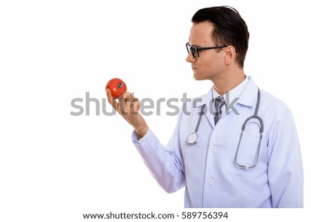 Profile view of young handsome man doctor holding red tomato