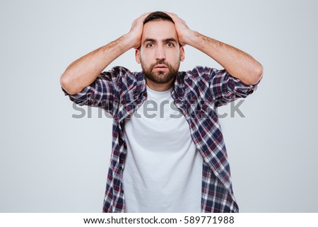 Shocked Bearded man in shirt which holding head and looking at camera
