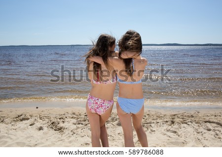Back view of two sisters girl teenager slim looking at the ocean