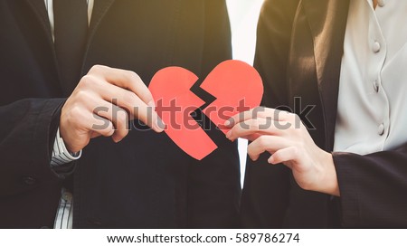 Man and woman pulling a red paper heart apart. The concept of unrequited love. Broken heart.