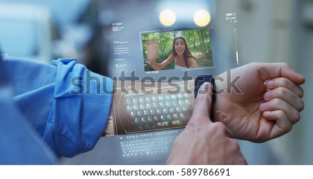 A man answers the wife who smiles and waves from the phone that appears in hologram clock futuristic and technological. Concept: network, communication,family, technology, augmented reality and future Royalty-Free Stock Photo #589786691