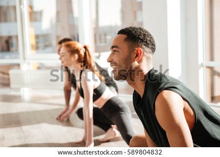 Cheerful african american young man doing yoga in group in studio