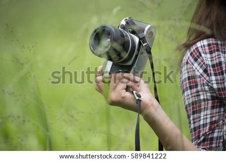 A beautiful girl wearing plaid shirt (red,black,white) ,holding the camera vintage ,with meadow in the morning.