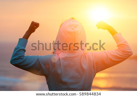 Back view of strong motivated woman celebrating workout goals towards the sun. Morning healthy training success. Royalty-Free Stock Photo #589844834