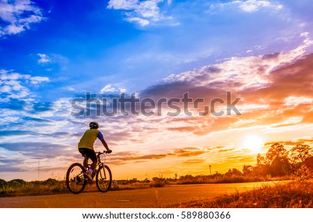 Cyclist ride bicycle at sunset with beautiful sky on background.