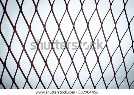 Close metal old rusty brown grille bars on white gray blue background. Abstract the universal background. Diamonds, geometry, weave, intersection.
