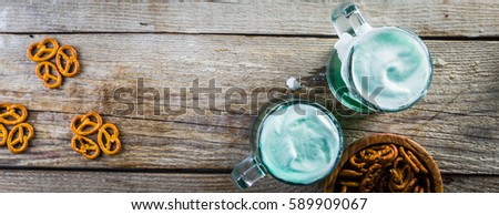Green beer in mugs and snacks on rustic wood background, copy space