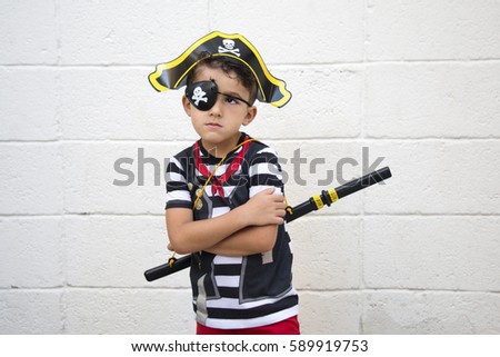 Little pirate boy is posing to the camera with crossed arms. Rustic wall background.