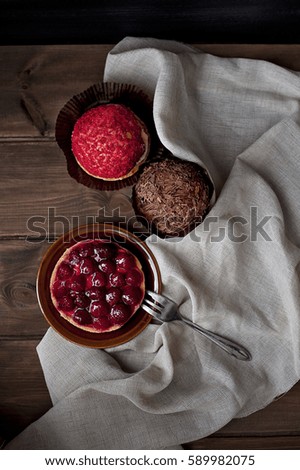 Composition of strawberry cake, chocolate muffin and red donut on a wooden table - dark food photography