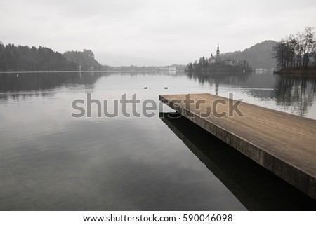 close up on empty wooden walkway on scenic lake bled with view on island in cloudy winter time, bled, slovenia