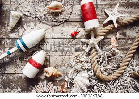 Styled composition with sea theme objects: fishing net, rope, buoy, float, starfish, shell, tackle, boat accessories on old wooden floor. Flatlay top view. Place for image or text. 