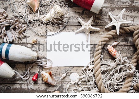 Styled composition with sea theme objects: fishing net, rope, buoy, float, starfish, shell, rope, tackle, boat and ship accessories and paper mock up. Flatlay top view. Place for image or text. 
