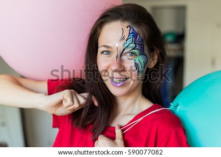Happy girl, young woman with braces and painted face in a festive mood with balloons. Face painting. Birthday party
