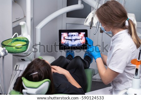 Healthy teeth. Female doctor dentist is showing x-ray teeth on tablet to young patient. Dentist or stomatologist is wearing medical clothing