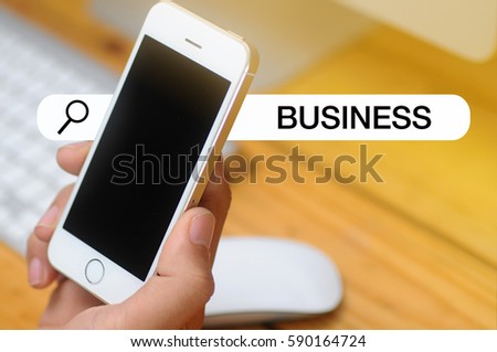 Smart phone in hand front of office equipment background and written BUSINESS. tone image