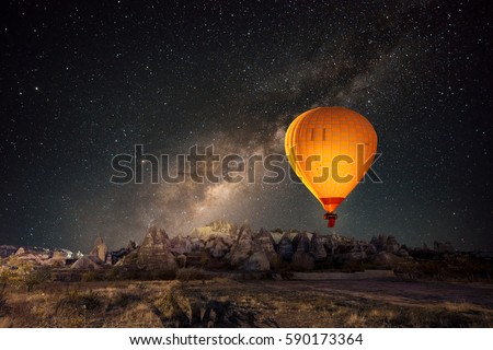 Hot air balloon flying over spectacular Cappadocia under the sky with milky way and shininng star at night (with grain) Royalty-Free Stock Photo #590173364