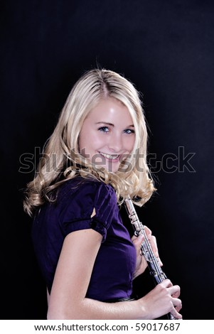A blond blue eyed teenage girl flute player isolated against a black background in vertical format.