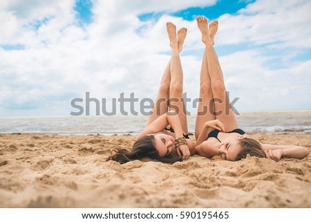 Two young girls in bikini swimsuit rest on the beach