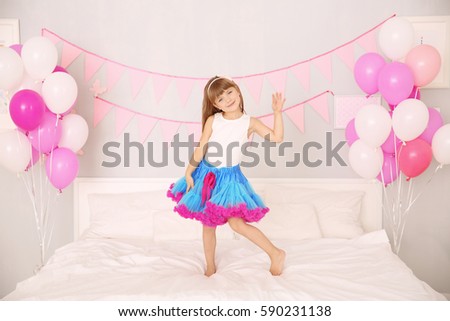 Cute girl standing on bed in room decorated for birthday celebration