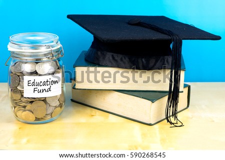 Coin in the jar with text education fund, books and graduation hat on wooden background.