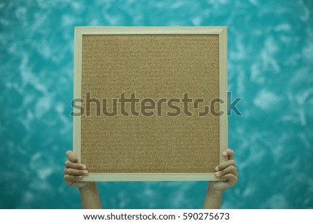Hands holding a blank wooden board on green abstract background with place for text.