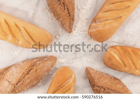 Loaves of rye and wheat bread with traces of flour, forming a frame on a white marble table with a place for text