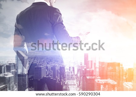 Rear view of a businessman holding his smartphone and looking at its screen. There is a cityscape in the background. Toned image. Double exposure.