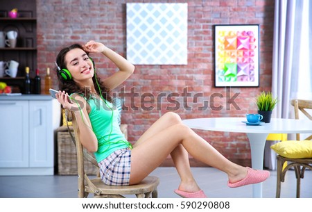 Happy young woman in headphones sitting on chair and listening to music