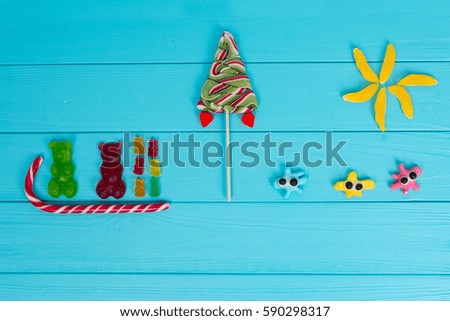 Funny picture of tasty jelly candies in the shape of bears sledging and trees on wooden turquoise table