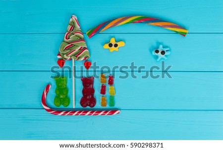 Cheerful picture of tasty jelly candies in the shape of bears sledging and trees on wooden turquoise table