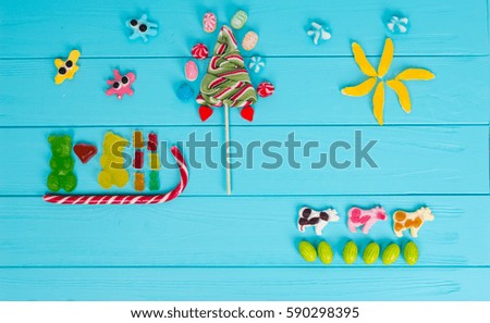 Funny picture of jelly candies in the shape of bears in love are sledging and trees on wooden turquoise table
