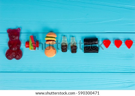 Delicious candies represent in the form of a gummy bear, burger and drink that is love on wooden turquoise table