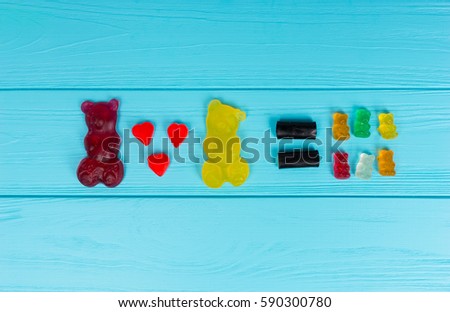 Tasty jelly candies represent that one big gummy bear plus a second equals a lot of little bears on wooden turquoise table