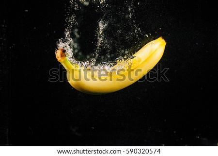 Sprkling yellow banana falls in water on black background
