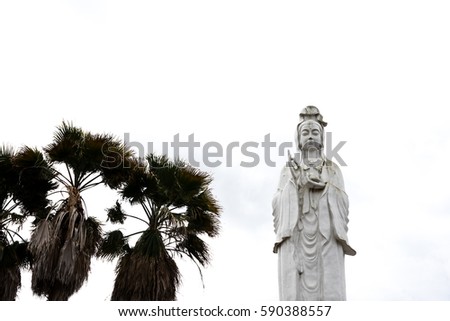 Low angle view of The Bodhisattva of Mercy, Goddess of Compassion, or Quan Yin / Guan Yin / Guan Yim in Houston, Texas, US. Majestic white Buddha statue with palm trees isolated on white background.