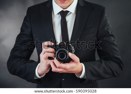 Business man holding black digital camera. In the studio on a dark background