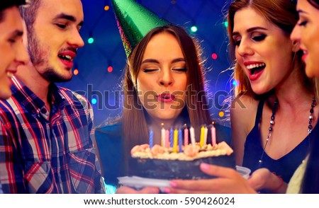 Happy friends birthday party with candle celebration cakes. People looking at burning candles. Two women and men have fun in nightclub.