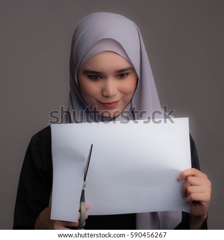 A pretty lady wearing hijab hold a piece of paper  a scissor on grey background.Business concept