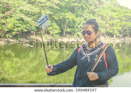 Asian woman is enjoy taking selfie picture by her own mobile phone and selfie stick in the park somewhere with the nice flare in the afternoon.