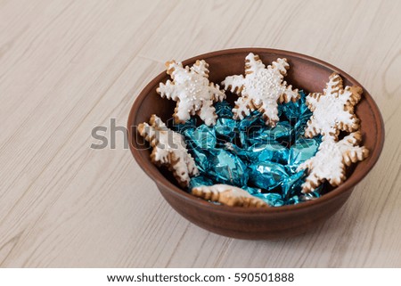 Gingerbread snowflake and bright candies in ceramic bowl on wood background.