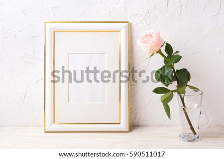 Gold decorated frame mockup with tender pink rose in glass. Empty frame mock up for presentation artwork.