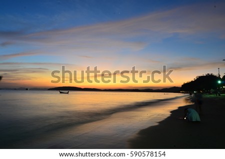 Silhouetted scenery of men and boats on sandy beach in Krabi, Thailand