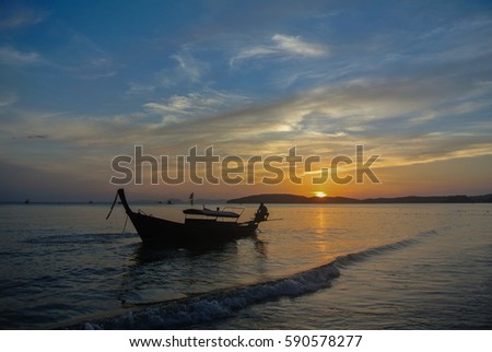 Silhouetted scenery of men and boats on sandy beach in Krabi, Thailand
