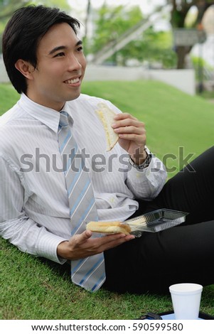 Businessman sitting on grass in park, having sandwich lunch