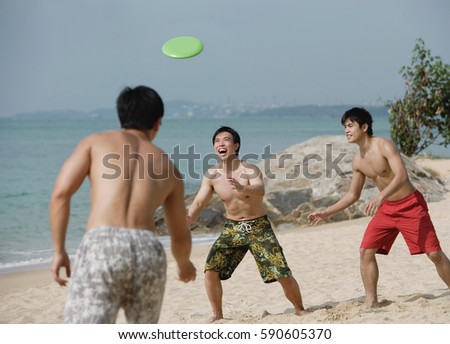 Three young men on beach playing with Frisbee