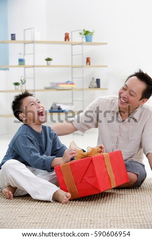 Father and son at home, boy opening gift, looking up