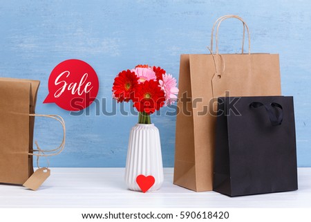 Mockup of blank shopping bags. Sale speech bubble. Gerbera flowers and red heart. Brown and black craft packages. Concept for sales or discounts. Blue wooden rustic board.
